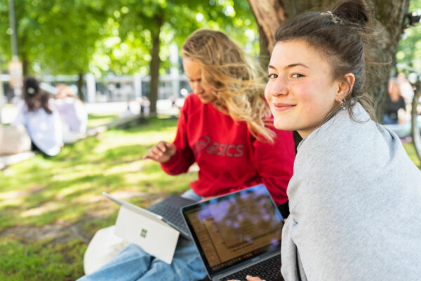 Studierende sitzen mit Laptops auf dem Campus